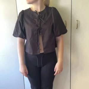 Svart blus med snörning från Gina Tricot - Säljer en svart  blus från Gina Tricot i storlek S. Toppen har korta puffärmar, croppad passform och snygg snörning framtill. Perfekt att styla med höga byxor eller kjol för en trendig look. Aldrig använt!!!!