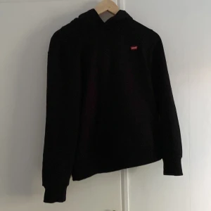 Svart hoodie från Levi's med huva - Svart hoodie från Levi's med klassisk röd logotyp på bröstet. Tröjan har huva och långa ärmar, passar en som är 164 ungefär skriv vid intresse 