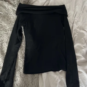 Svart offshoulder topp från Pieces - Säljer en svart offshoulder topp från Pieces med långa ärmar och ribbad struktur. Toppen har en tight passform och är perfekt för dig som gillar en stilren och enkel look. Snygg att matcha med både jeans och kjol.