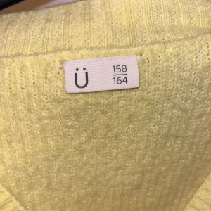 Gul ribbad kofta från Ü, croppad - Superfin ljusgul kofta från Ü med croppad passform och stora knappar framtill. Ribbstickad i mjukt material och med lång ärm och v-ringad hals. Perfekt att slänga över en topp för en chill look.