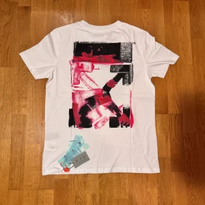 Vit Off-White t-shirt med tryck - Vit t-shirt från Off-White med coolt grafiskt tryck i svart och rött på ryggen och mindre tryck framtill. Klassisk rund hals och korta ärmar. Materialet är mjuk bomull och passformen är normal. Perfekt för dig som gillar streetwear och snygga detaljer.