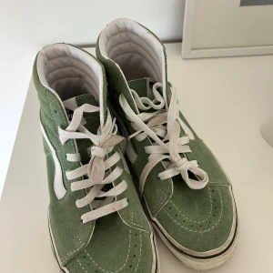 Gröna Vans Sk8-Hi sneakers - Snygga gröna Vans Sk8-Hi sneakers med vit sula och klassisk vit sidestripe. Skorna har snörning, rund tå och är tillverkade i mocka och canvas. 