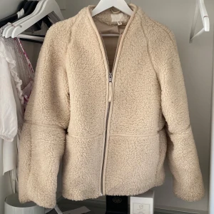 Beige teddyjacka med dragkedja - Mysig beige teddyjacka med hel dragkedja framtill och långärmade ärmar. Jackan har en fluffig och mjuk känsla, perfekt för kyliga dagar. Enkel och stilren design som passar till många outfits. Jackan är från hm 