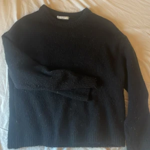 Svart stickad tröja från Gina Tricot - Mysig svart stickad tröja från Gina Tricot med rund halsringning och ribbade muddar. Perfekt för lager-på-lager och passar till allt. Tröjan är i en klassisk modell med lång ärm och känns både enkel och stilren. Använd sparsamt så fint skick.