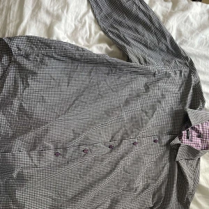 Svartvit rutig skjorta från Stomberg 2XL - Snygg svartvit rutig skjorta från Stomberg i storlek 2XL. Skjortan har lila knappar och ett coolt lila/vitt rutigt mönster på insidan av kragen. Regular fit med lång ärm, perfekt för dig som gillar klassisk stil med en twist.