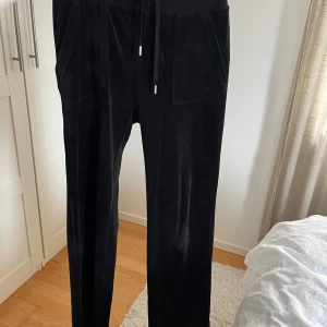 Svarta mjukisbyxor i sammet - Svarta mjukisbyxor från Juicy Couture i mjuk sammet med dragsko i midjan och stora fickor fram och bak. Byxorna har raka ben och en broderad JC-logga på ena byxfickan.