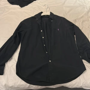 Svart skjorta från Ralph Lauren - Säljer en stilren svart skjorta från Ralph Lauren i slim fit. Skjortan har långa ärmar och knappar framtill. Perfekt för en elegant look.