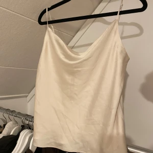 Beige satinlinne från H&M - Säljer ett elegant beige satinlinne från H&M. Linnet har tunna axelband och en mjuk, glansig yta som ger en lyxig känsla. Perfekt för att klä upp en outfit eller bära som det är🩷