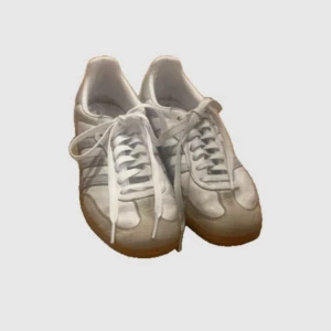 Vita Adidas Samba sneakers - Säljer ett par klassiska vita Adidas Samba sneakers med ljusbruna sulor och de ikoniska tre ränderna i grått på sidan. Skorna har snörning och är perfekta för en sportig look. Storlek 36. Finns defekter så skriv för bilder på dom. Pris kan diskuteras❤️