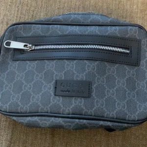 Grå axelväska från Gucci - Snygg grå axelväska från Gucci med ett diskret mönster och en praktisk dragkedja framtill. Väskan har en elegant design och är perfekt för att bära dina nödvändigheter med stil. Den kommer med en skyddande dustbag.