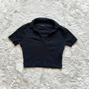 Croppad pikétröja  - Snygg svart croppad pikétröja . Toppen har en klassisk krage och korta ärmar, perfekt för en stilren look. Passar bra till både jeans och kjol.