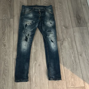 Blå jeans från Dsquared2 - Säljer ett par coola blå jeans från Dsquared2 med slitna detaljer och en vintage look. Jeansen har en knappgylf och klassisk femficksdesign. Perfekta för en avslappnad stil. storlek 30/32