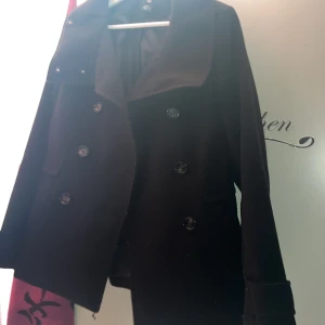 Svart kappa från H&M - Snygg svart kappa från H&M med klassisk krage. Perfekt för kyligare och varmare dagar och ger en stilren look. Perfekt nu för våren. Passar bra till både vardag och mer uppklädda tillfällen.