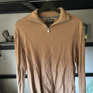 Beige tröja med dragkedja från Jack & Jones - Säljer en stilren beige tröja från Jack & Jones med halv dragkedja vid halsen. Tröjan har långa ärmar och är perfekt för en avslappnad look. Tillverkad i ett mjukt material som känns skönt mot huden.