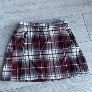 Rutig kjol från MAMALICIOUS - Snygg rutig kjol i vinrött och grått från MAMALICIOUS. Kjolen har dragkedjor framtill och är fodrad med ett svart innerfoder. Perfekt för en stilren look!