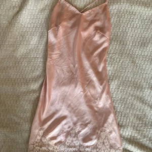 Slipdress - Ljusrosa klänning i siden-aktigt material från Hunkemöller med spetsdetaljer längst ner. Klänningen har smala sjusterbara axelband, ger en så fin passform. En liten fläck (se sista bild). Ej testat om den går bort i tvätt.