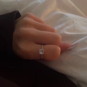 Elegant silverring med stor sten - Säljer en elegant silverring med en stor, gnistrande sten i mitten. Ringen har en smal banddesign med små stenar längs sidorna som ger extra glans. Perfekt för speciella tillfällen eller som en vacker accessoar till vardags.