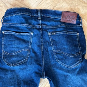 Mörkblå jeans från Lee - Säljer ett par mörkblå jeans från Lee med klassisk femficksdesign och knappgylf. Perfekta för en avslappnad stil. W30 L30