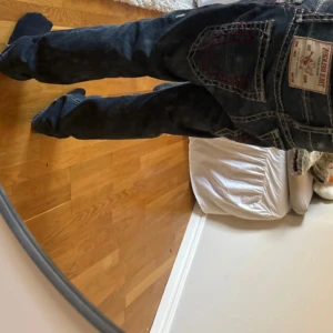 Mörkblå jeansbyxor från True Religion - Säljer ett par mörkblå jeansbyxor från True Religion med unika broderade detaljer på bakfickorna. Byxorna har en klassisk femficksdesign och en bekväm passform. Perfekta för dig som vill ha en stilren och trendig look. (Pris går att diskutera)