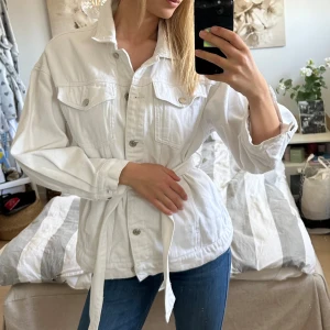 Vit jeansjacka med knytband - Snygg vit jeansjacka med knytband i midjan och knappar framtill. Säljs då den inte kommer till användning längre. 💕