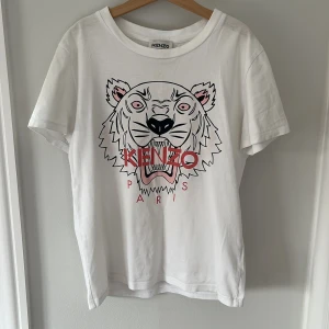 Vit t-shirt med tigertryck från Kenzo - Säljer en cool vit t-shirt från Kenzo med ett stort tigertryck i svart och rosa på framsidan. T-shirten har korta ärmar och rund halsringning. Frakt ingår inte i priset!