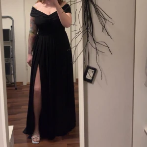 Svart långklänning med slits - Elegant svart långklänning med offshoulder-design och en djärv slits. Klänningen har en v-ringad överdel med rynkade detaljer som ger en smickrande passform. Aldrig använd💕