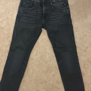 Mörkgråa jeans från Replay - Snygga mörkgråa jeans från Replay i modellen Anbass. De har en slim passform och är tillverkade i ett stretchigt material för extra komfort. Klassisk femficksdesign med dragkedja och knapp framtill.