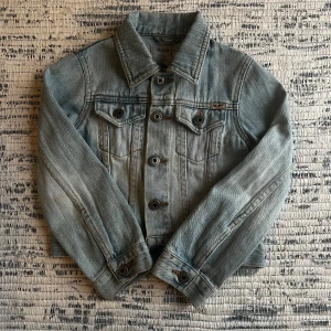 Ljusblå jeansjacka från Marina Duester - Snygg ljusblå jeansjacka från Marina Duester med klassisk design och knappar framtill. Jackan har två bröstfickor med knapp och en  signaturdetalj på sidan från Yumi och Tomu. Pris kan diskuteras och kontakta mig för mer information!