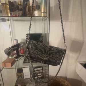 Axelväska från Zadig & Voltaire - Snygg svart limit edition axelväska från Zadig & Voltaire med coola nitar i ett mönster på framsidan. Väskan har en kedjerem som ger en rockig känsla. Perfekt för att ge din outfit en edgy touch.