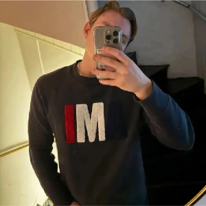 Mörkblå tröja med bokstäver - Säljer en mörkblå tröja med stora bokstäver i rött och vitt på framsidan. Tröjan har långa ärmar och en rund halsringning. Perfekt för en avslappnad stil.