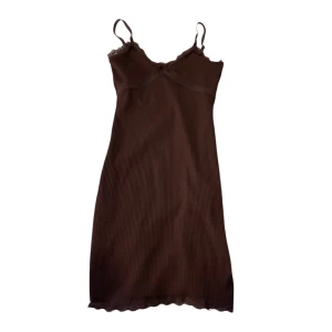Brun ribbad klänning - Säljer en brun ribbad klänning med smala axelband och spetsdetaljer vid bysten. Klänningen har en figurnära passform och är perfekt för en stilren look.