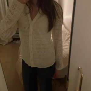 Vit spetskofta från VILA - Säljer en elegant vit spetskofta från VILA. Koftan har ett vackert spetsmönster och långa ärmar. Perfekt för att lägga till en romantisk touch till din outfit. Den har en knappstängning framtill och är i storlek S.