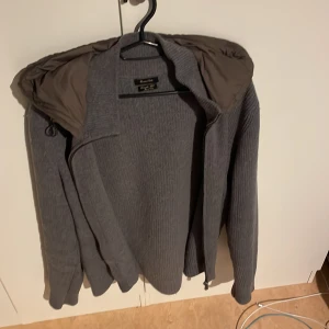 Massimo dutti cardigan  - Säljer en stilren grå stickad jacka från med dragkedja och en quiltad huva. Jackan har långa ärmar och en ribbad struktur som ger en snygg look. Perfekt för kyliga dagar! Köpte den för 1900 o säljer för 1800. Knappt använd skick 9/10 Inga defekter. Säljer för den va lite för stor! Kom pm för mer info. 