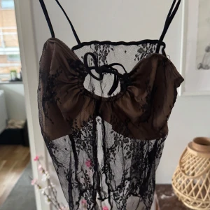 Svart spetslinne med rosett - Säljer ett elegant svart spetslinne med tunna axelband och en söt rosett framtill. Perfekt för en kväll ute eller en speciell tillställning. Linnet har ett transparent mönster som ger en sofistikerad look.