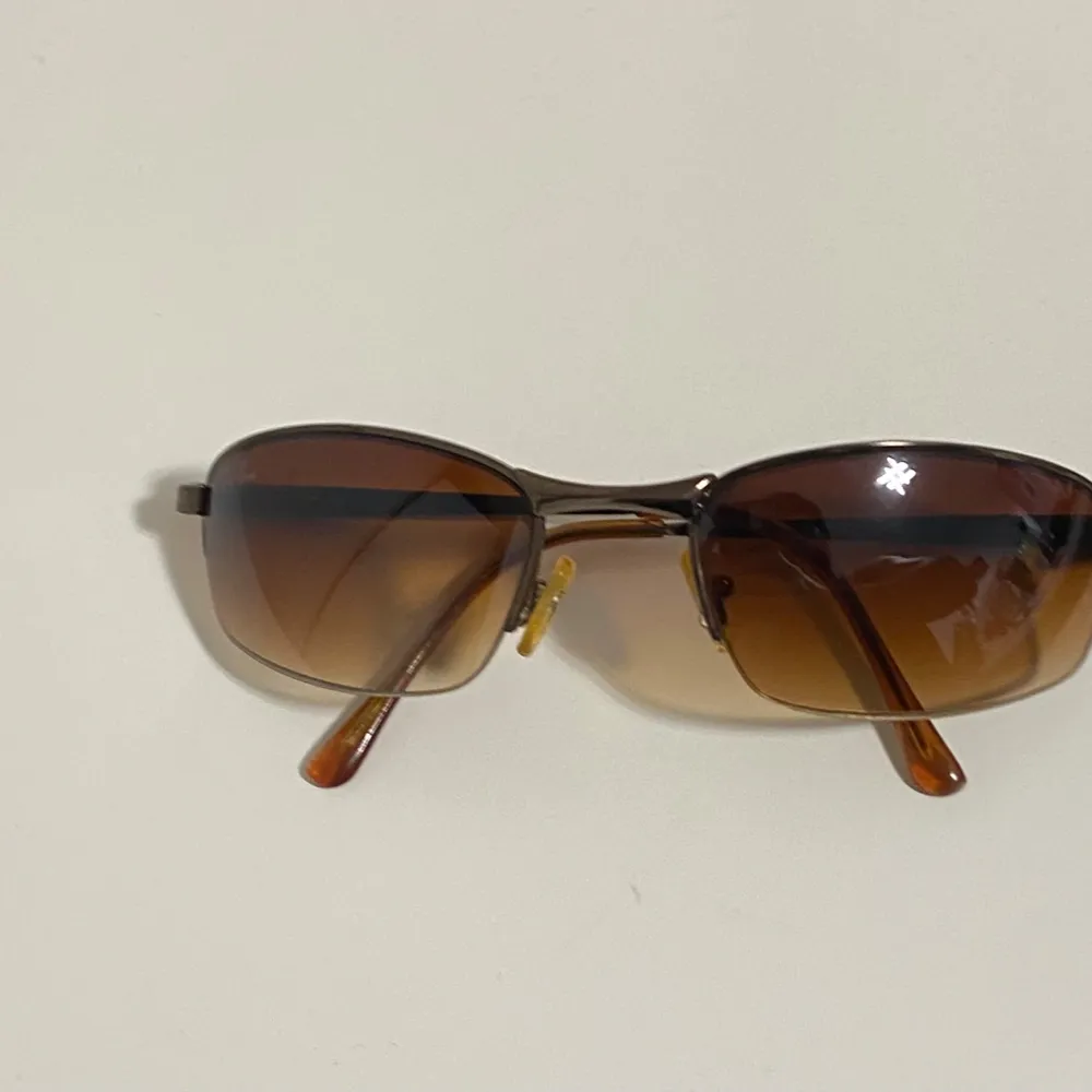 Snygga bruna solglasögon från Ray-Ban med en elegant design. De har en halvram och tonade glas som ger ett stilrent intryck. Perfekta för soliga dagar och kommer med ett praktiskt fodral.. Muu.