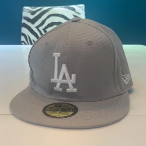 Grå keps från New Era - Snygg grå keps från New Era med broderad LA-logga. Helt ny då jag aldrig andvänt den, kan vara lite vikt pga att ja haft den i garderoben. Perfekt att komplettera din outfit speciellt nu till sommaren. Hör av er vid intresse🤩