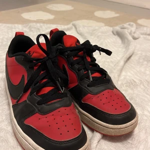 Nike sneakers i rött och svart - Snygga Nike sneakers i en klassisk röd och svart färgkombination. Skorna har en låg profil med svart snörning och en vit sula. Perfekta för en sportig look. Lite lortiga på sulorna men det fixas lätt innan det skickas! Priset kan sänkas!