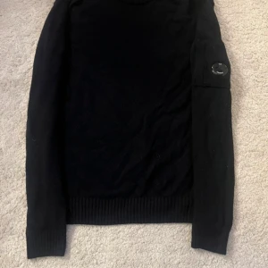 Svart fleece tröja från C.P. Company - Säljer en stilren svart fleece tröja från C.P. Company. Tröjan har långa ärmar ochp en snygg detalj med en logotyp på ärmen. Perfekt för kyligare dagar.