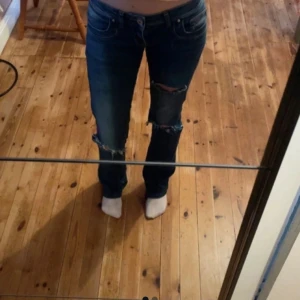Mörkblå Ltb jeans med låg midja och slitningar - Lågmidjade LTB jeans med hål på knäna och låret. Långa på mig som är 177cm.