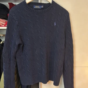 Mörkblå stickad tröja från Polo Ralph Lauren - Säljer en snygg mörkblå stickad tröja från Polo Ralph Lauren med kabelstickat mönster. Tröjan har långa ärmar och en rund halsringning. Perfekt för kyliga dagar! Storlek S men har blivit mer som XS