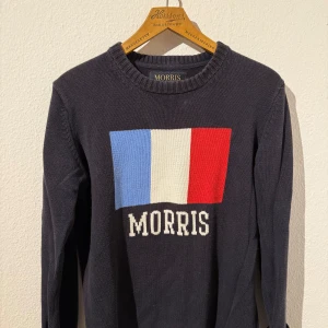 Morris stickad tröja med tryck - Snygg mörkblå stickad tröja från Morris med stort tryck i blått, vitt och rött på bröstet samt Morris-logga. Storlek S