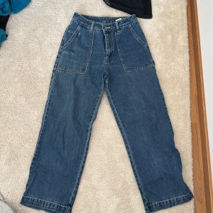 Wide jeans från Monki, blå, storlek 26 - Säljer ett par blå jeans från Monki i storlek 26. Modellen är wide med hög midja, fast man kan använda som låg midjat. Jeansen har stora fickor fram och bak samt en cool detalj på sidan. Tillverkade i 100% bomull för en skön och klassisk jeanskänsla.