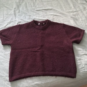 Vinröd stickad kortärmad tröja - Säljer en vinröd stickad tröja med korta ärmar och rund hals. Tröjan har en loose passform och är gjord i ett stickat material Perfekt för dig som gillar enkla och stilrena plagg med lite extra cozy vibe.