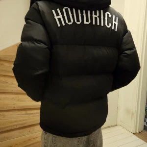 Svart pufferjacka från Hoodrich S - Säljer en svart pufferjacka från Hoodrich i storlek S. Jackan har stor logga på ryggen och mindre logga fram, dragkedja och huva. Fodrad och riktigt tjock, perfekt för kalla dagar. Snygga detaljer med Hoodrich-band på insidan.