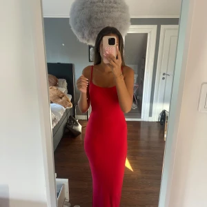 Röd långklänning med smala axelband - Säljer en röd långklänning med smala axelband och figurnära passform. Klänningen har en enkel och stilren design med rundad halsringning och ärmlös modell. Perfekt för dig som gillar en clean look och vill sticka ut med färg.