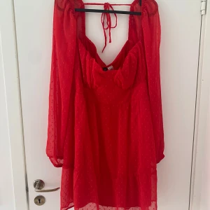 Röd kortklänning med puffärmar  - Superfin röd kortklänning från H&M med puffiga långärmar och knyt i nacken. Klänningen har ett diskret prickigt mönster och volang nedtill. Materialet är lätt och luftigt, perfekt för att sticka ut. Söt urringning och markerad midja ger en snygg siluett.