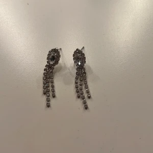 Glittriga silverörhängen med strass - Säljer ett par snygga örhängen i silverfärg med glittrande strass. De har en oval form upptill och tre hängande rader av strass som ger extra bling💞