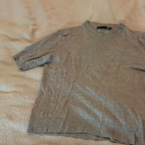 Grå stickad tröja från 157, S - Snygg grå stickad tröja från 157 i storlek S. Tröjan har korta ärmar och rund hals med ribbad kant. Perfekt för dig som gillar enkel och clean stil. Materialet är mjukt och skönt, och den neutrala färgen gör den lätt att matcha med allt. Den är sydd då den haft ett hål, inget som man tänker på!💞