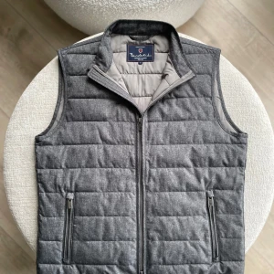 Grå quiltad dunväst från Bondelid - Snygg grå dunväst från Bondelid med quiltad design och ståkrage. Västen har två fickor med dragkedja och hel dragkedja framtill. Perfekt att slänga över en hoodie eller tröja för extra värme. Klassisk och stilren look som funkar året runt. 10/10 skick! Storlek M.