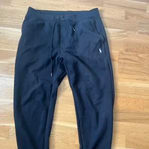 Svarta mjukisbyxor från Polo Ralph Lauren - Svarta mjukisbyxor från Polo Ralph Lauren med klassisk logga broderad på ena benet. Byxorna har dragsko i midjan och är tillverkade i mjukt bomullsmaterial. Perfekta för chill dagar eller när du vill vara bekväm men ändå se snygg ut.